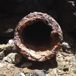 a rusty pipe sitting on top of a pile of rocks